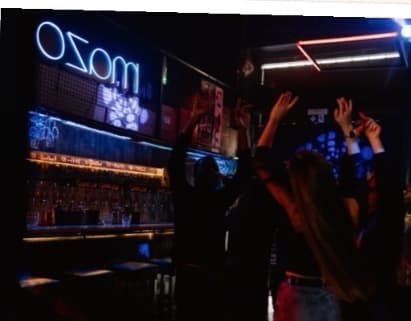 Guests dancing with their arms up in front of a neon bar sign, in black and white