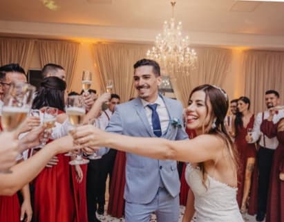 Wedding guests in red dresses raising champagne glasses with the couple